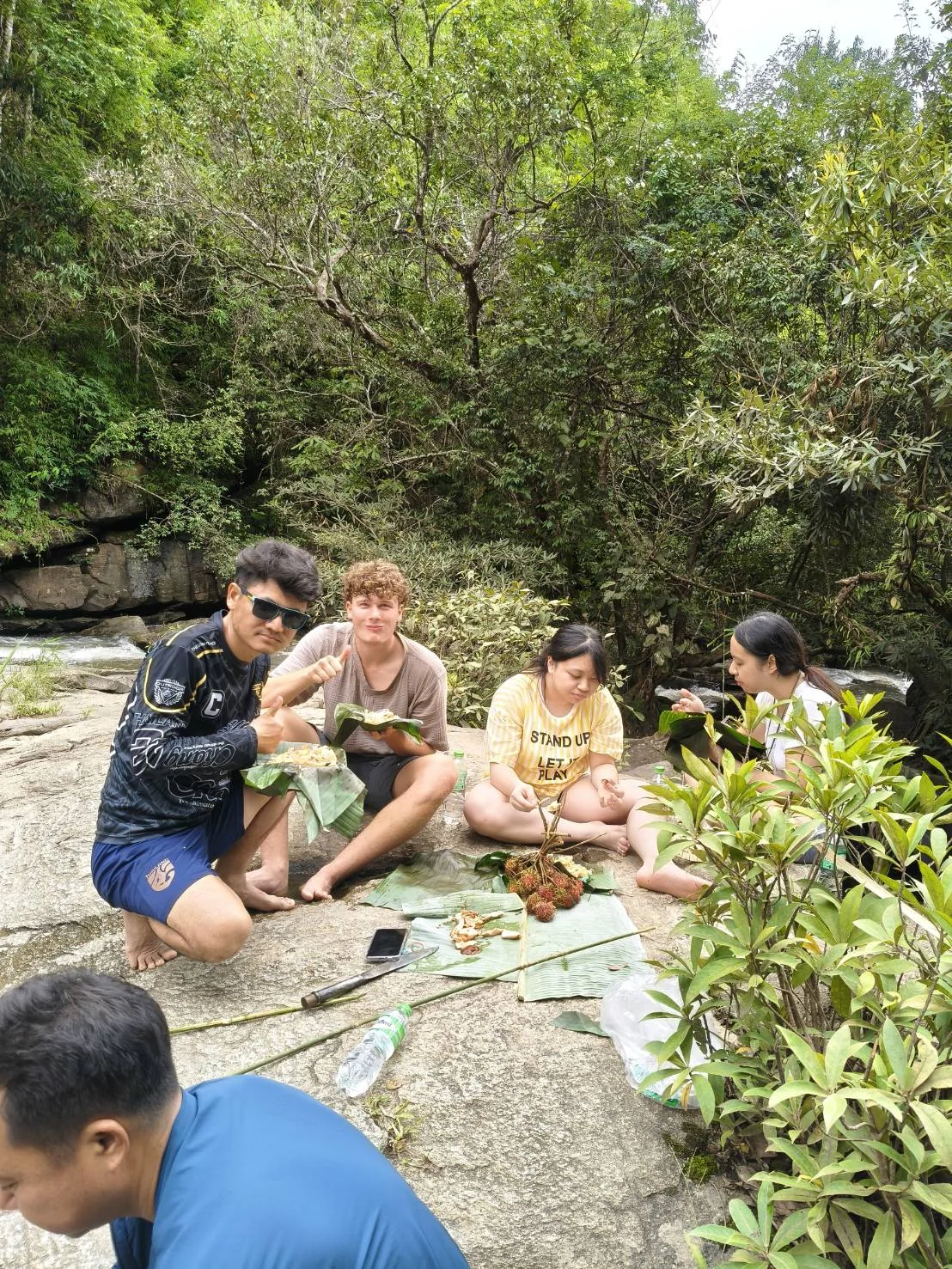 Travellers sharing a meal served on banana leaves near a waterfall